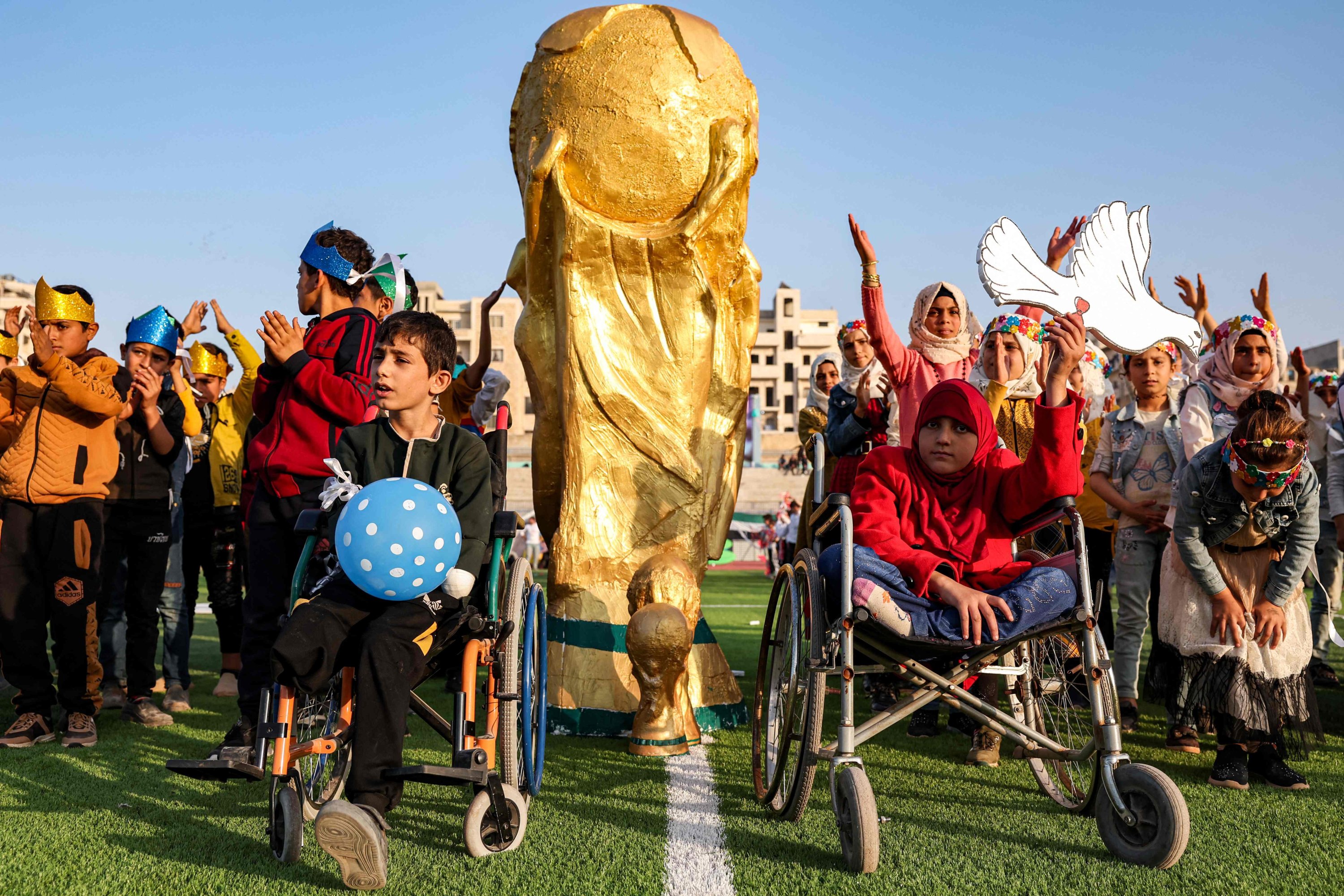 Tekerlekli sandalye kullananlar da dahil olmak üzere çocuklar, Dünya Kupası'nın açılış töreninde sahada FIFA Dünya Kupası kupasının bir maketinin önünde poz veriyor. 