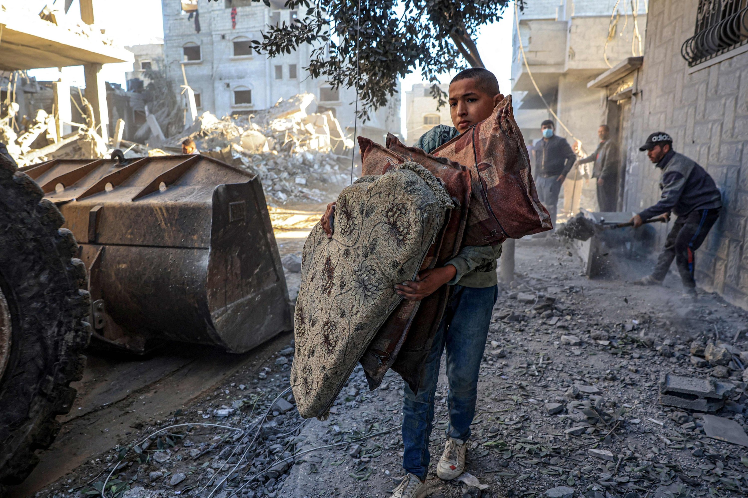 Filistinli bir çocuk, İsrail bombardımanlarında yıkılan binaların enkazını traktörle temizlerken yastık taşıyan Filistinli bir çocuk, Gazze Şeridi'nin güneyindeki Refah'ta, Filistin, 15 Aralık 2023. (AFP Fotoğrafı)